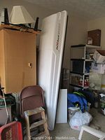 White Yakima RocketBox roof cargo box shell standing upright leaning against a wall alongside furniture and storage items in garage.