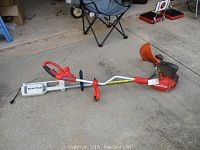 Side profile of Black & Decker Grass Hog trimmer laid on concrete floor with folding chair and other items in background.