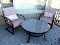 Front view of two metal frame chairs with cushions and a round glass topped table on a porch.