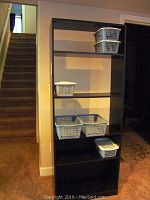 Front view of tall black particle board bookshelf with plastic baskets in place, showing some wear.