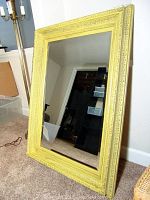 Front view of decorative yellow framed wall mirror leaning against wall on carpeted floor.