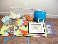 Full view of children's bedroom decor lot items arranged on colorful quilt on carpet. Items include quilt with letter M pattern, two wire shelves, piggy bank, framed dolphin pencil art, books, and small figurines.