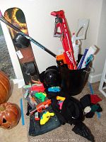 Wide view of snowboard standing up with attached bindings, black helmet, various water guns and Nerf guns, black gloves, knit hat and scarf, and a blue and white hockey stick.