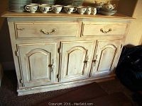 Front view of distressed whitewash wood buffet with two drawers and three cabinet doors, showing wear and scratches.