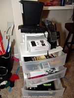 Photo of large plastic organizer with three transparent drawers, small plastic organizer with three drawers on top, paper shredder, and vertical file organizer with thermoses on the floor.