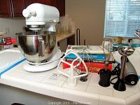 KitchenAid stand mixer with stainless steel bowl, wire whips, flat beater, dough hook, immersion blender and cookbooks on kitchen counter