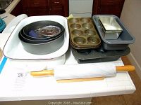 Photo showing all baking pans including roasting pan, round pans, muffin pans, bread pans, rectangular pan, and rolling pin with stand on a kitchen counter.