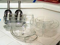Photo showing three clear glass serving trays including a round divided tray on a stand, an oval tray with handle, and a rectangular tray, also two rectangular glass butter dishes with lids.