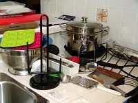 Overall kitchen countertop view showing stainless steel pot with steamer, colander, ice cube trays, and various utensils