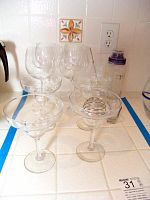 Photo showing four margarita glasses, four wine glasses, and a glass with lid and coil stirrer on counter
