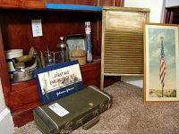 Wide view of lot showing first aid kit, irons, washboard, framed Americana print, and stoneware crock.
