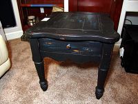Side view of the distressed black and teal wooden table with single drawer and decorative legs