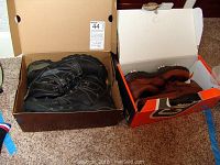 Both pairs of shoes inside their respective shoeboxes, Keen boots in brown box, FootJoy golf shoes in orange and black box.