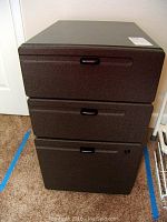 Front view of brown 3-drawer metal file cabinet showing all closed drawers and black handles.