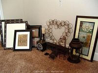 Photo of all items in lot grouped on carpet against wall: four frames, two framed artworks, metal lantern, candle holders, heart-shaped metal wall art, metal box, and metal shelf.