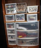 Front view of multiple plastic drawer storage bins stacked on shelving, containing sewing supplies including spools of thread, ribbons, and other craft materials.