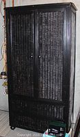 Front view of wood and wicker armoire with two drawers, black painted frame and woven wicker panels.