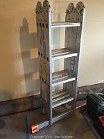 Photo of the folded Krause MultiMatic aluminum ladder standing vertically showing its rungs and orange safety feet caps.