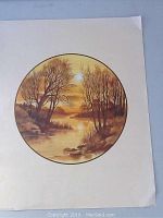 Image of unframed circular lithograph print on paper showing natural landscape with leafless trees and river in golden yellow/brown tones.