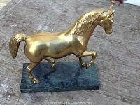 Front angle view of the polished brass horse sculpture mounted on the green marble base, showing the horse's raised front leg and detailed mane and tail.