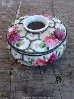 Porcelain dish with lid on top, showing the floral hand-painted design and three legs.