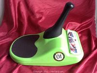 Mini luge toboggan showing side profile, green plastic with black handle and seat, featuring '01' sticker and informational label.