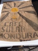 Front view of the jute coffee bag showing the Cafe Solar Honduras print with a sun graphic and steaming coffee cup.