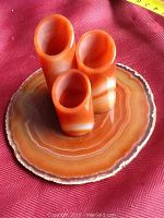 Side view showing three natural carnelian pencil holders of varying heights, polished and cylindrical, mounted on a polished circular agate base with natural band patterns.