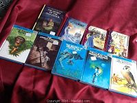 10 hardcover books with colorful illustrated dust jackets including Hardy Boys, Nancy Drew, and other classic titles arranged on red fabric.