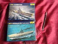 Two unopened Heller model ship kits stacked one on top of the other on a red surface with a pen for scale. The top box is 1/750 Clemenceau, the bottom box is 1/600 Arromanches.
