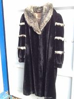 Full view of the faux fur coat showing the black body with raccoon-style lighter fur trim on collar and sleeves.