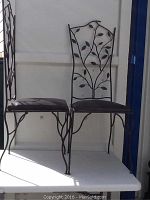 Two black leather seat wrought iron chairs with decorative leaf pattern backs shown from front and side