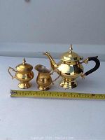 Photo of the assembled brass tea set with a measuring tape beneath for scale