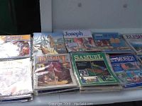 Stacked Bible lesson workbooks on various biblical figures Joseph, Daniel, Samuel, and others, packaged in plastic envelopes