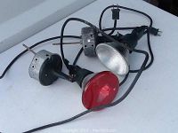 Two electric floodlights, one with a red glass reflector and one with a clear glass reflector, showing cords and plugs, overall condition and wear on the red reflector