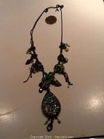 Full view of the 16-inch green costume jewelry necklace with dark metal chain, floral and bead details, next to a coin for scale.