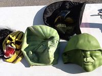 Four Halloween masks laid out on a white surface: pumpkin demon, green goblin, green hooded mask, black hooded grim reaper mask.