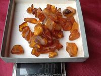 Close-up photo of loose natural amber beads on a weighing scale, showing total weight of 28 grams.