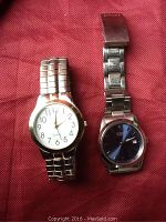View of two men's wristwatches side by side on a red fabric background. Citizen watch has a blue dial and Montre Carlo a white dial.