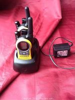 Two Motorola walkie talkies in yellow and black in a charging dock with a power adapter placed on a red fabric background.