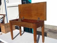 Full view of the solid wood piano bench with open hinged seat showing interior storage compartment and sturdy legs.