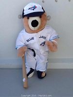 Front standing view of Blue Jays teddy bear in full baseball uniform holding wooden bat.