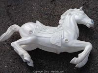 White plastic carousel horse on asphalt with detailed molded saddle and mane, showing mounting holes and surface wear