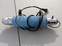 Side view of the lamp showing the blue ribbed glass body, chrome caps, electrical cord and plug wrapped around it.