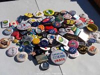 Photo showing a large pile of assorted vintage badges spread out on a plain surface. Various shapes and colors visible.