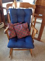 Front view of wooden Boston rocker with blue seat cushion, two red plaid throw pillows placed on it.