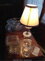 Multiple clear beaded glass pieces and milk glass lamp on wooden table with lamp turned on