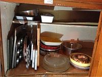 Overview of different baking pans and cookie sheets stacked inside a cupboard