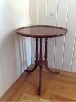 Photo of round occasional table showing top surface and three carved legs with tripod base, wood finish, slight wear visible.