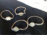 Photo of 4 vintage ladies watches on black cloth showcasing various round and rectangular watch faces with metal bands.